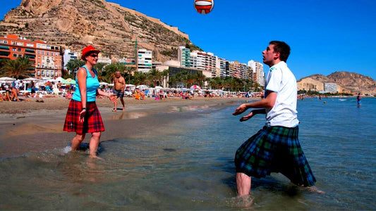 Couple playing football also they wearing kilts.